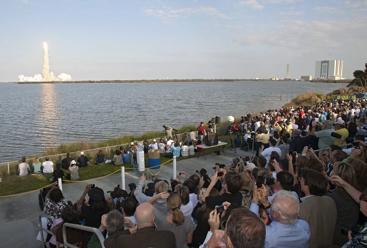 A crowd watching a Space Shuttle launch from across the water